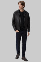 font pose pocket Full-length studio shot of a male model wearing a modern, slim-fit black leather hooded bomber jacket over a black t-shirt and dark blue jeans against a solid white background.