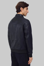 Front studio shot of a man wearing a slim-fit black leather bomber jacket with a snap-tab collar and zippered pockets, styled with dark pants against a white background.