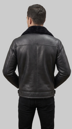 A man viewed from behind wearing a black leather jacket with a dark shearling-style collar, paired with black pants, against a plain gray studio background.