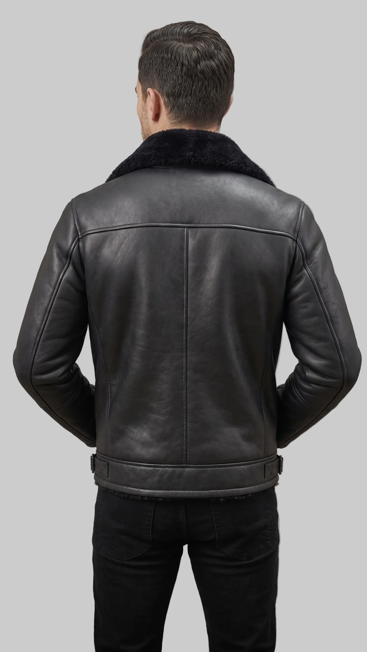 A man viewed from behind wearing a black leather jacket with a dark shearling-style collar, paired with black pants, against a plain gray studio background.