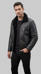 A man wearing a black leather jacket with a black sherpa collar, styled over a black t-shirt and black jeans, standing against a gray studio backdrop.