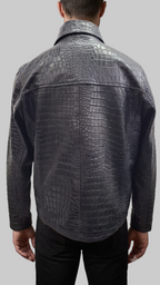 A man viewed from the back wearing a dark gray crocodile-embossed leather jacket and black trousers, standing against a textured gray studio backdrop.