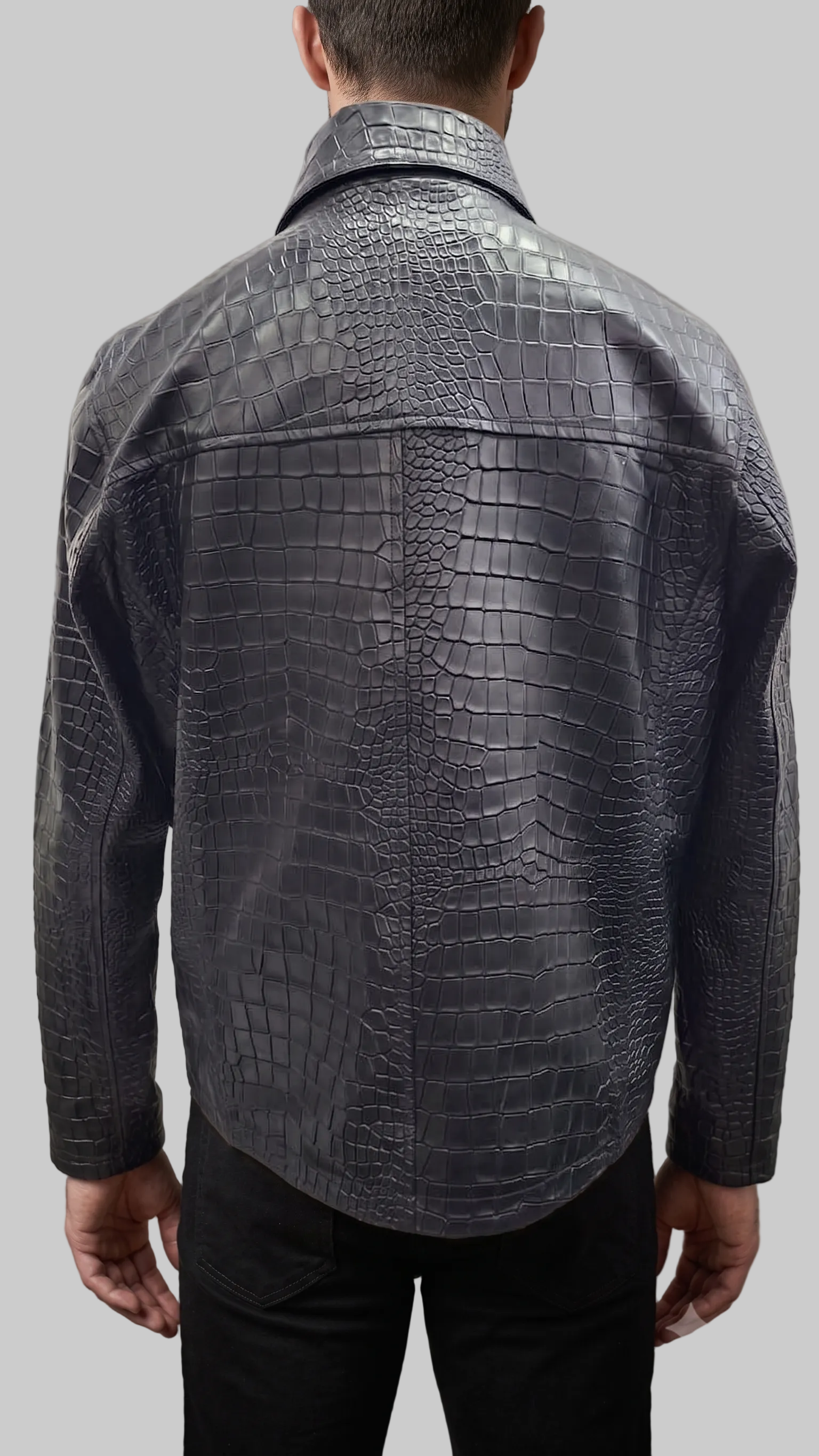 A man viewed from the back wearing a dark gray crocodile-embossed leather jacket and black trousers, standing against a textured gray studio backdrop.