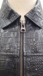 Close-up of a black crocodile-embossed leather jacket with a silver metal zipper, displayed on a beige mannequin torso.