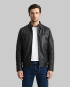 A man wearing a black leather motorcycle jacket over a white t-shirt and blue jeans, standing against a plain white studio background.
