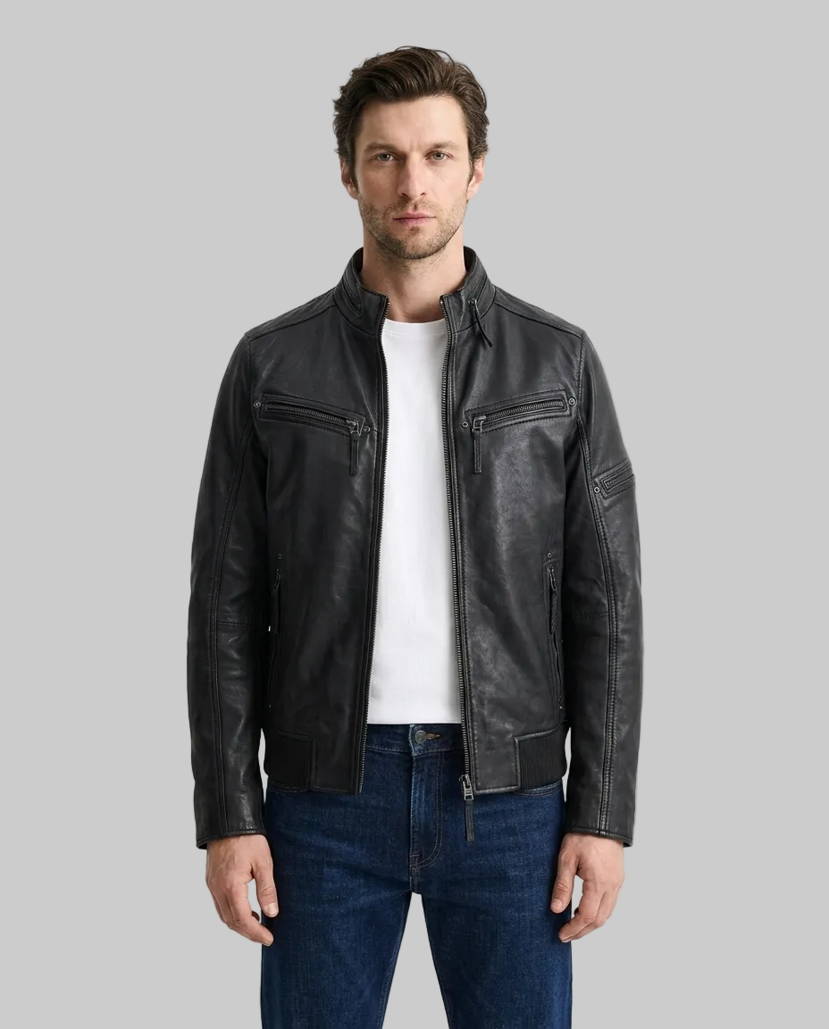 A man wearing a black leather motorcycle jacket over a white t-shirt and blue jeans, standing against a plain white studio background.