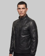 A man wearing a black leather jacket with multiple zippered pockets, photographed against a plain white studio background.
