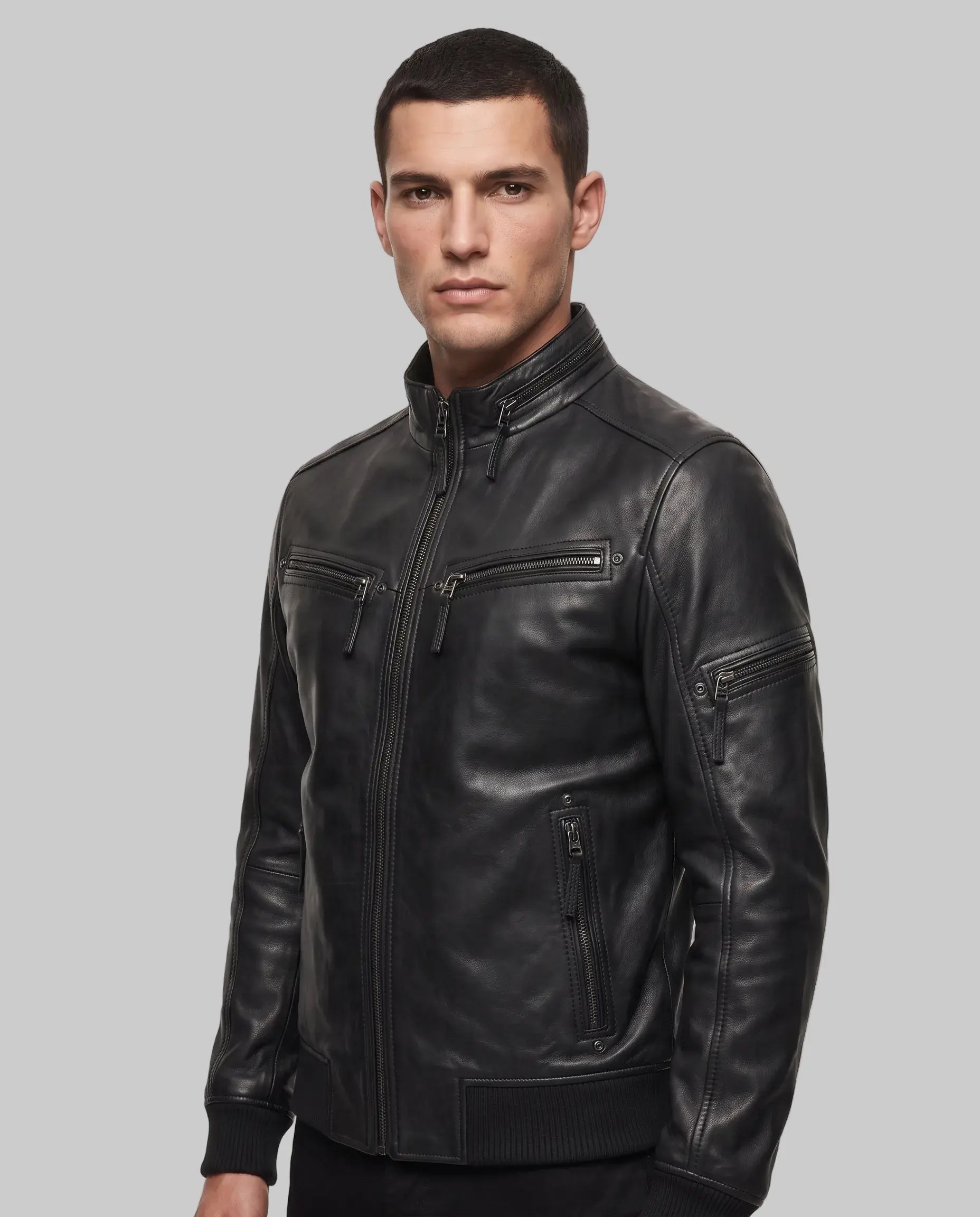 A man wearing a black leather jacket with multiple zippered pockets, photographed against a plain white studio background.