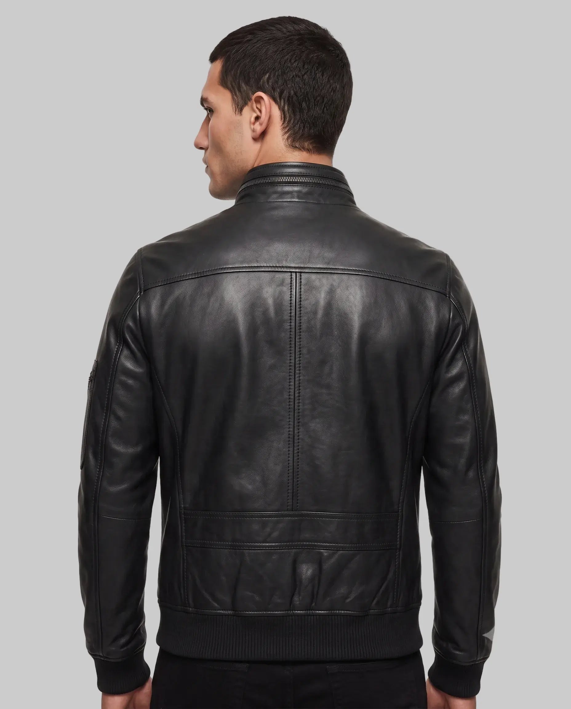 A man viewed from the back wearing a black leather jacket with a ribbed knit collar, cuffs, and hem, set against a plain white studio background.