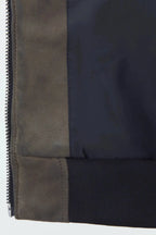 Close-up detail of a patchwork jacket showing a dark navy nylon body, a taupe-brown suede panel, and a black ribbed knit cuff with a silver zipper.