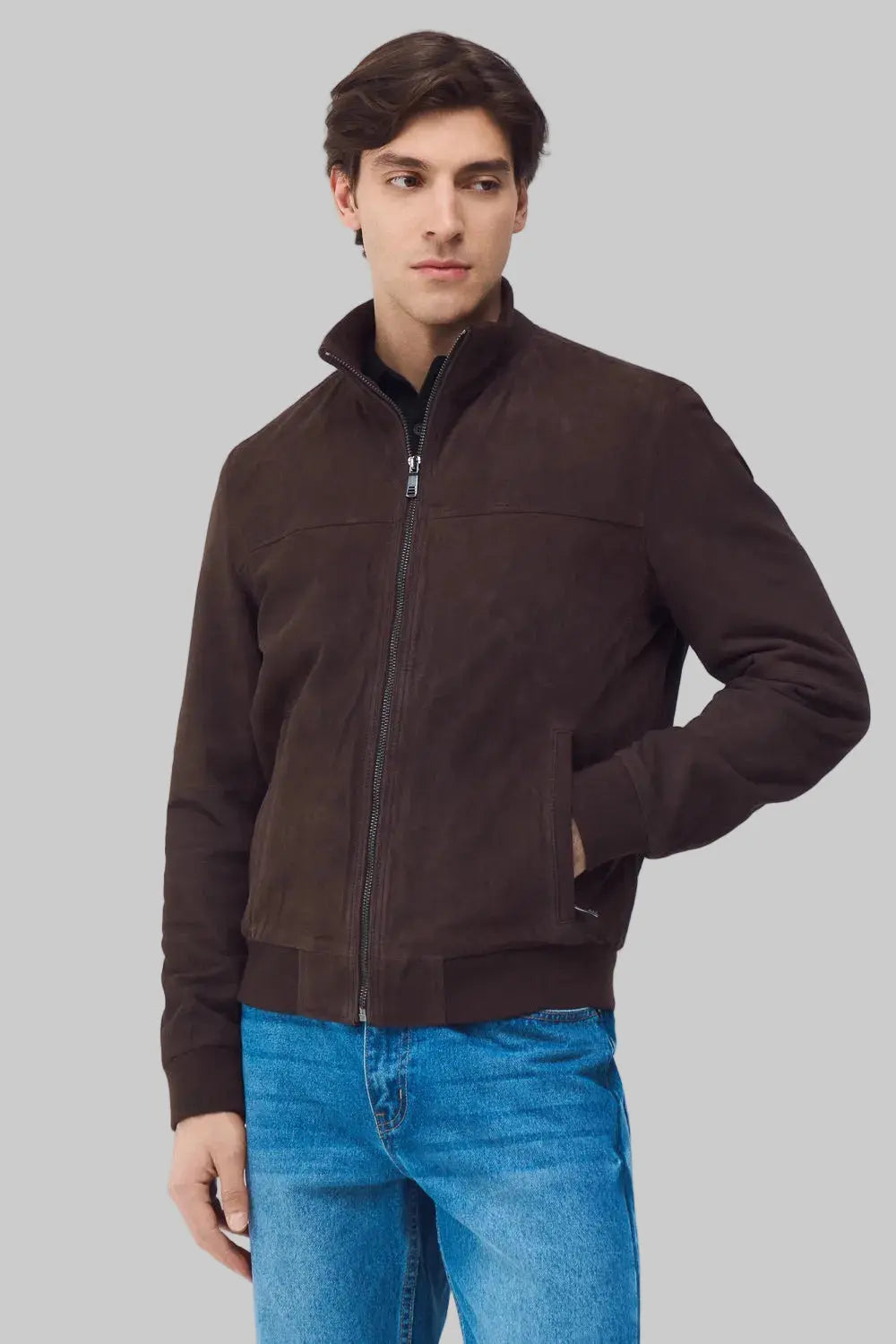 Man wearing a brown jacket and blue jeans on a light gray background