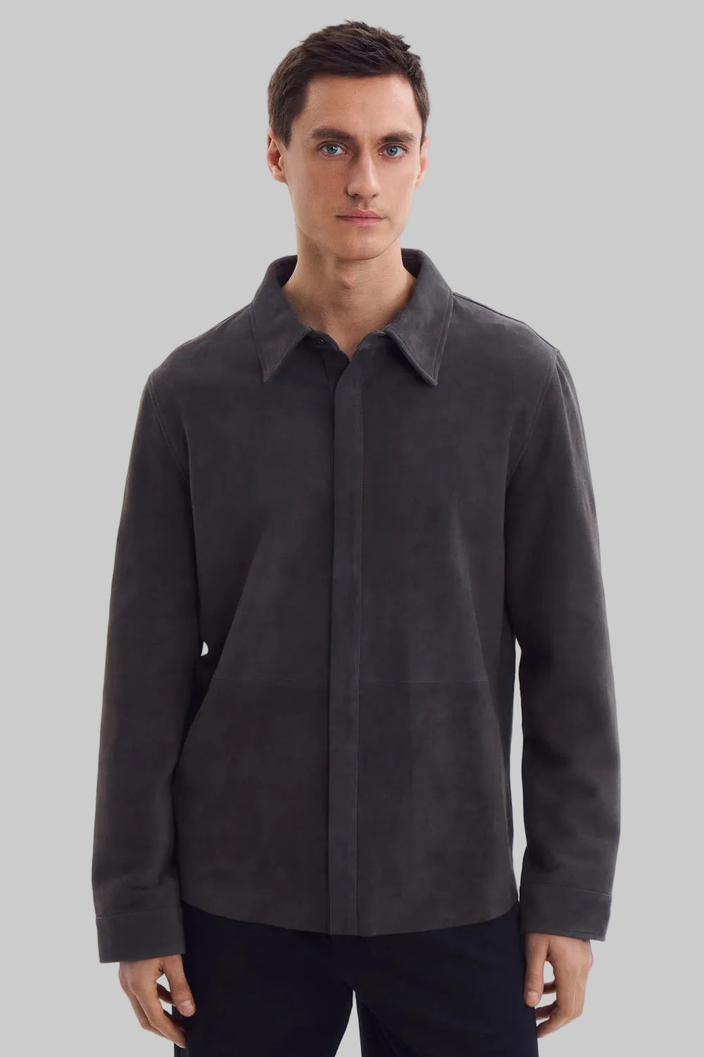 Front studio portrait of a man wearing a minimalist, charcoal gray suede shirt jacket snapped completely closed, featuring a clean concealed placket and point collar against a solid white background.